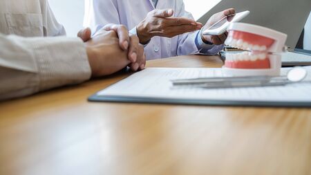 Dentist showing and explaining teeth disease treatment to patient using teeth model denture and...