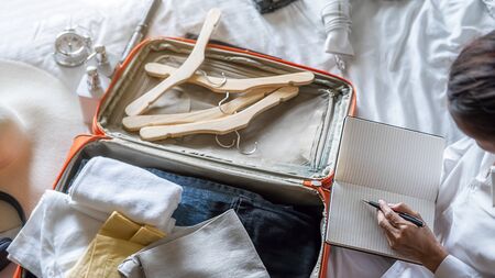 Preparation for vacation or travel. Happiness young woman packing a clothes and stuff into opened suitcase on bed.の写真素材
