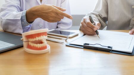 Dentist showing and explaining teeth disease treatment to patient using teeth model denture and...