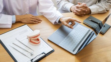 Dentist showing and explaining teeth disease treatment to patient using teeth model denture and...
