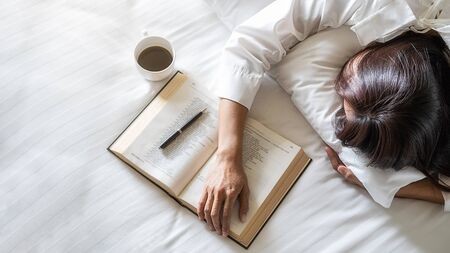Asian tired woman lying on the bed after read a book in the morning with soft morning light. Morning...