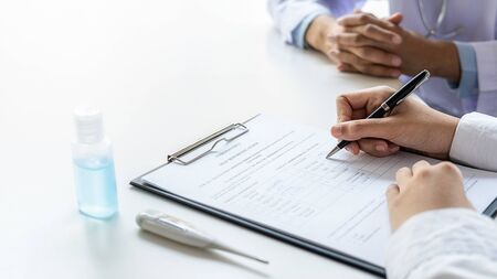 Asian woman filling a coronavirus self reporting form with a doctor recommended at hospital. Medical and Health concept.の写真素材