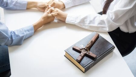 Christian woman praying with hands together on holy bible and wooden cross. Woman pray for god...