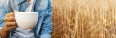 Asian woman holding cup of coffee and sitting in barley field on summer. Relaxing concept.の写真素材