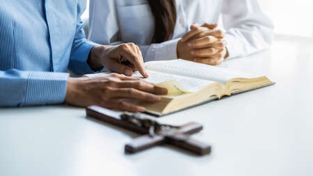 Christian woman praying with hands together on holy bible and wooden cross. Woman pray for god...
