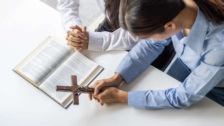 Christian woman praying with hands together on holy bible and wooden cross. Woman pray for god blessing to wishing have a better life and believe in goodness.の写真素材