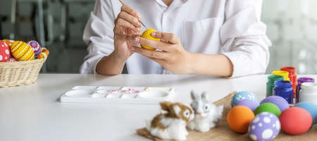 Happy Asian woman painting eggs for Eastertime at home. Family preparing for Easter.