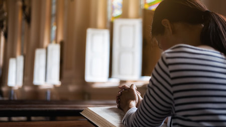 Christian woman praying on holy bible in the public church. Woman pray for god blessing to wishing have a better life and believe in goodness.の写真素材