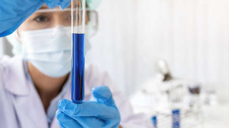 Scientist looking at test tube with clear solution in pharmaceutical research laboratory.
