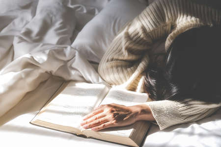 Asian tired woman lying on the bed after read a book in the morning with soft morning light. Morning lifestyle concept.の写真素材