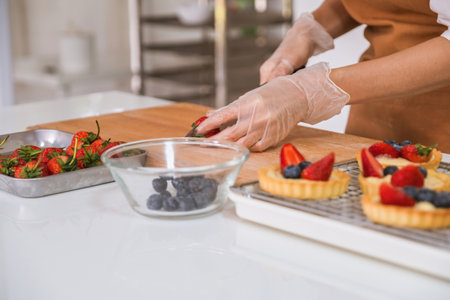 Mid section of woman cutting strawberry on tartlets in kitchen at homeの写真素材