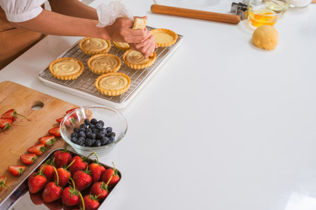 Close-up of woman preparing strawberry tartlets in kitchen at home