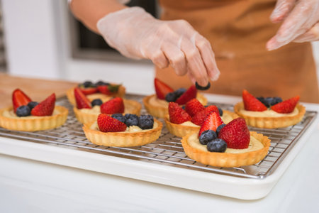 Close-up of female hands putting fresh berries on tartlets in the kitchenの写真素材