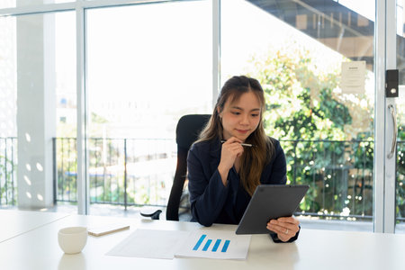 Businesswoman sitting at desk working on laptop and analyzing data on charts and graphs and writing on papers to make business plan and strategies.の写真素材