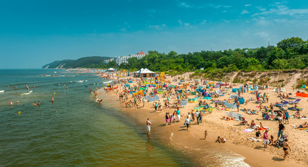 Miedzyzdroje / Poland - 07.11.2011: Lots of people on the sandy beach sunbathing, swimming in the sea, relaxing. Blue sky, sunny weather, summer season,のeditorial素材