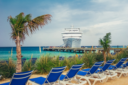 Grand Turk / Turks and Caicos Islands - May 10.2007: View on the Cruise Ship dock by the sandy beach full of blue sun beds and palm trees. Turquoise color sea, cloudy sky.のeditorial素材