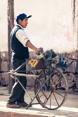 Cusco / Peru - May 27.2008: Man, key maker, locksmith standing on the street with the vintage, retro key making machine, device with one wheel and bunch of keys attached to it. Daytime, sunny.のeditorial素材