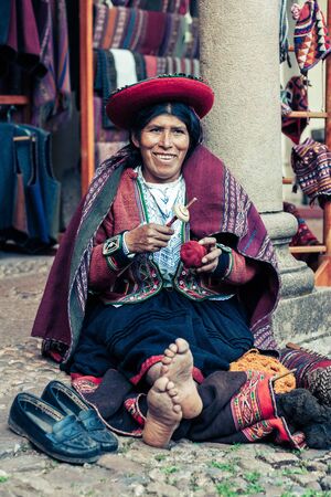 Cusco / Peru - May 26.2008: Portrait of a sewer woman, seamstress, dressed up in traditional native peruvian clothes. Seating on the street with barefoot, holding sewing tools while smiling.のeditorial素材