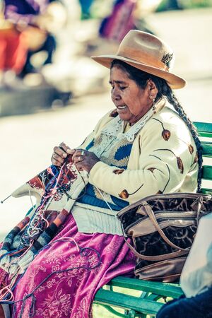 Cusco / Peru - May 26.2008: Portrait of a  indigenous woman, dressed up in traditional native peruvian clothes and hat. Seating on the bench holding the sewing tools during the sunny day.のeditorial素材