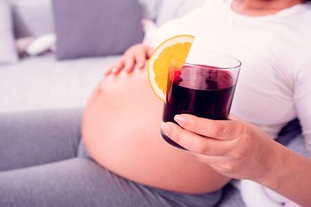 Pregnant woman enjoying her healthy organic green beetroot juice while relaxing on the couch at home.の写真素材