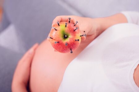 Pregnant woman eating apple stuffed with wood nails to increase iron level in the blood. Old...