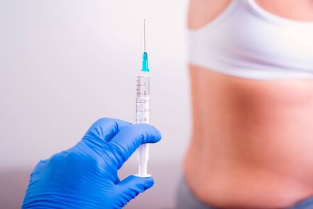 Pregnant woman having medicine injection. Hand with blue gloves holding syringe in front of the pregnant belly.の写真素材