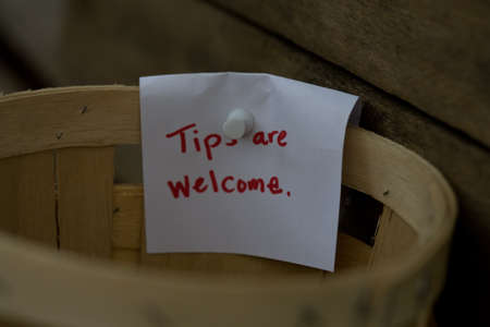 Handmade sign on wooden basket that spells Tips are welcome. Close-up with full frame rustic wood backgroundの写真素材