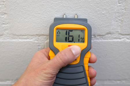 A male hand holding a yellow moisture meter in front of a wallの写真素材