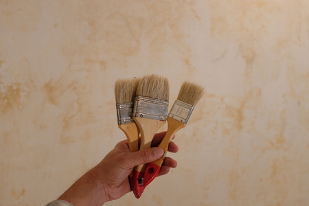 Detail of a male hand with paintbrush in front of a wall with torn off wallpapers