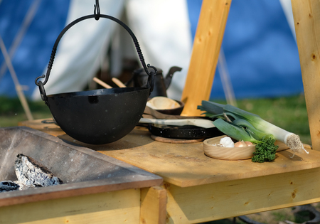 A rustic pot next to a fire pit with fresh ingredientsの写真素材