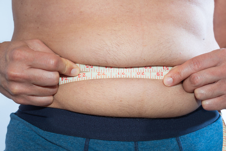 A slightly overweight man measures his waistの写真素材