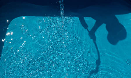 The shadow of a child with garden hose while filling the swimming pool