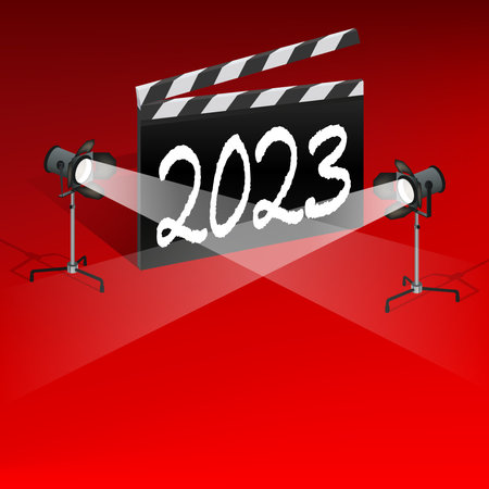 A cinema clapperboard on a red background with the inscription 2023. It is illuminated by two...