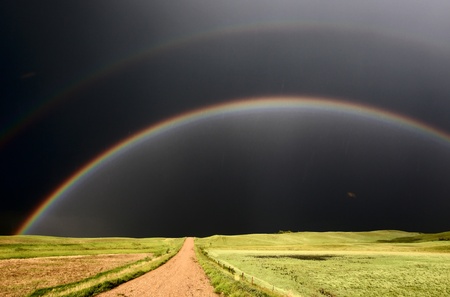 Rainbow and darkened skies seen down a country roadの写真素材