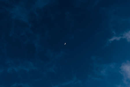 Minimal photo of Moon and white clouds in the evening dusky dark blue sky.