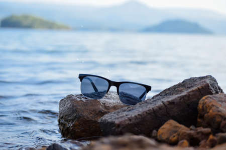 Sun glasses on rocks at the shore of lake with blue fresh water and blue hills layers during day with. used selective focus.の写真素材