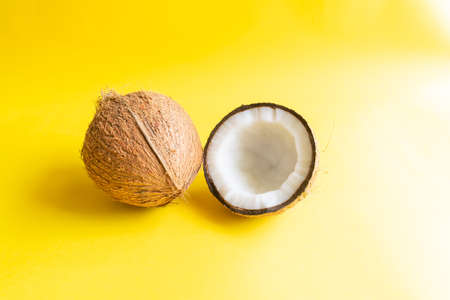Coconut of which husk removed and one half side of the coconut with shell on the yellow colored background and used selective focus.の写真素材
