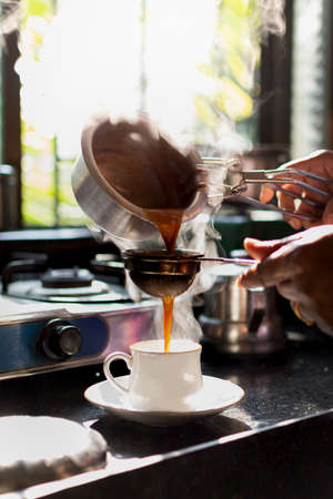 Woman hands Pouring tea in the white cup during morning time. Sunlight coming from the window. Steam...