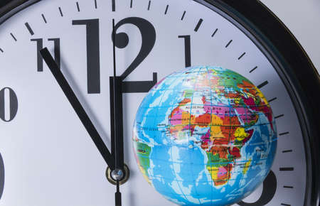 black clock with black digits and white dial behind a small colorful globe shows five to twelveの写真素材