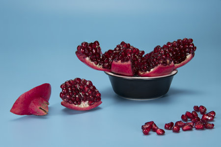 Pomegranate sliced and served in black bowl on light blue backgroundの写真素材