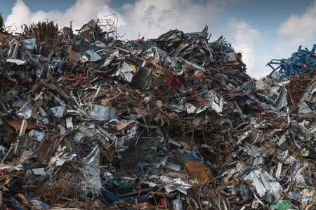 piled up iron scrap on scrap yard against blue partly cloudy skyの写真素材