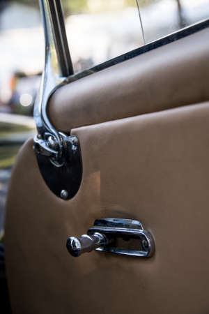 Close up of the inside of a door of a classic car with brown leather and chrome handlesの写真素材