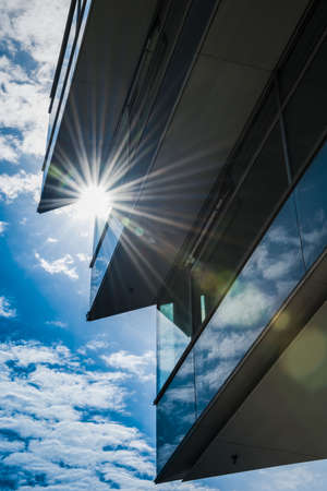 glazed facade of office building against the sun with slightly cloudy blue skyの写真素材
