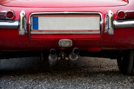Partial view of the rear of a classic red sports car with taillights and empty EU license plateの写真素材