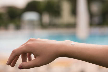 Arm and hand of young woman on vacation with sunscreen on arm and blue pool in backgroundの写真素材