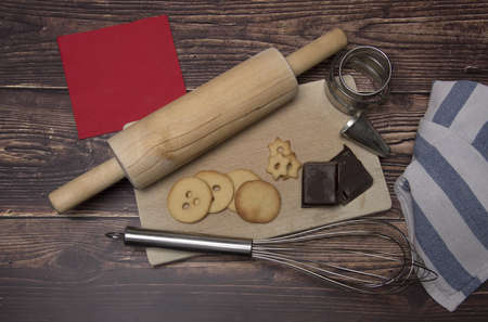 Wooden board with baking utensils cookies and cooking chocolate rolling pin whisk and baking dish isolated on dark wooden backgroundの写真素材