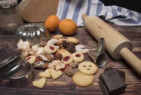 closeup of various christmas cookies like vanilla cookies with various baking utensils cookie cutters whisk and rolling pin on dark wooden backgroundの写真素材