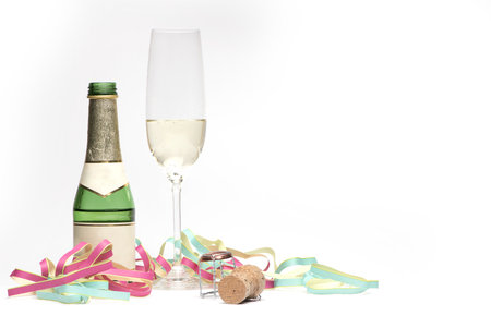 small champagne bottle next to half full champagne glass with party garlands for New Year's Eve on white backgroundの写真素材