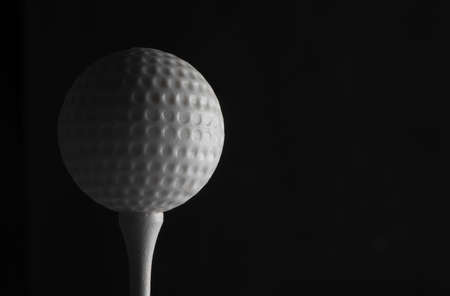 Close up low key photo of white golf ball on white tee isolated against black backgroundの写真素材