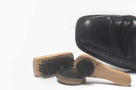 Closeup of black leather shoe next to shoe shine tools brushes shoe polish as concept for clean shoes leather care and shine isolated on white backgroundの写真素材